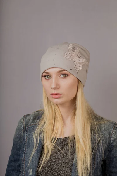 Retrato de una hermosa joven en un elegante tocado con maquillaje natural sobre un fondo gris . — Foto de Stock