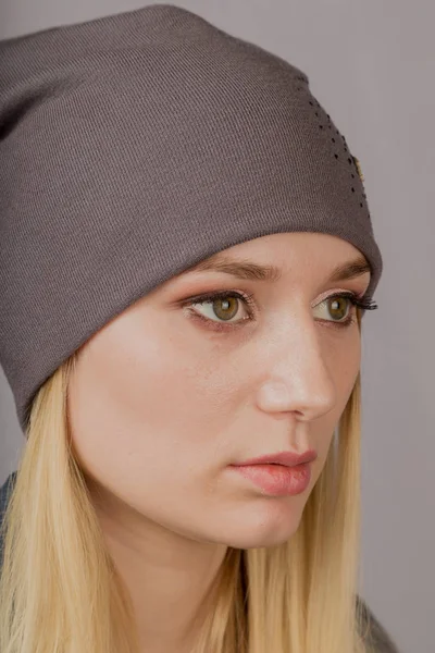Porträtt av en vacker ung flicka i en snygg huvudbonad med naturlig makeup på en grå bakgrund. — Stockfoto