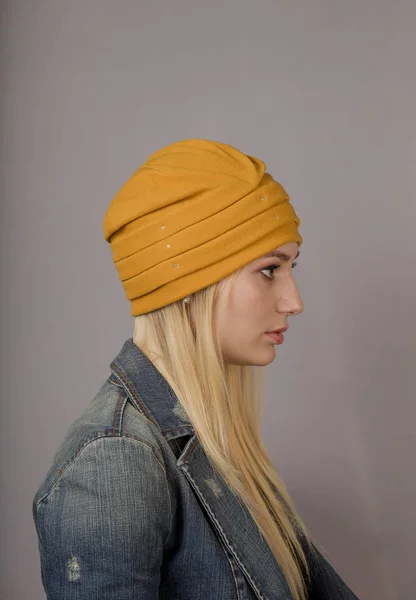 Portret van een mooi jong meisje in een stijlvolle hoofdtooi met natuurlijke make-up op een grijze achtergrond. — Stockfoto