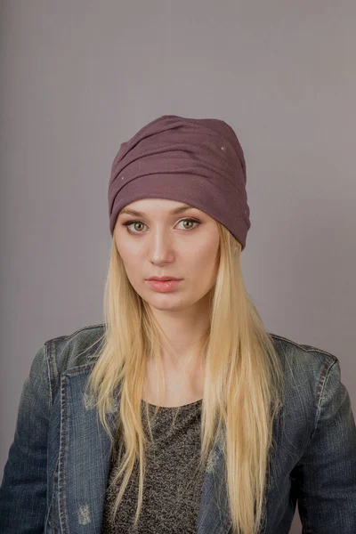 Portret van een mooi jong meisje in een stijlvolle hoofdtooi met natuurlijke make-up op een grijze achtergrond. — Stockfoto