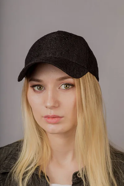 Portret van een mooi jong meisje in een stijlvolle hoofdtooi met natuurlijke make-up op een grijze achtergrond. — Stockfoto