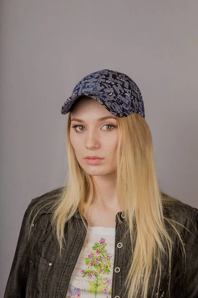 Portret van een mooi jong meisje in een stijlvolle hoofdtooi met natuurlijke make-up op een grijze achtergrond. — Stockfoto