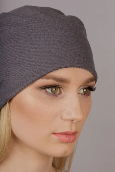 Menina bonita com maquiagem natural em uma cobertura para a cabeça em um fundo cinza . — Fotografia de Stock