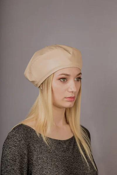 Retrato de uma bela jovem em uma cobertura para a cabeça elegante com maquiagem natural em um fundo cinza . — Fotografia de Stock