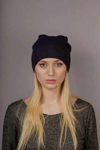 Portret van een mooi jong meisje in een stijlvolle hoofdtooi met natuurlijke make-up op een grijze achtergrond. — Stockfoto