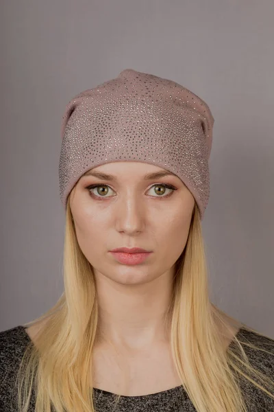 Portret van een mooi jong meisje in een stijlvolle hoofdtooi met natuurlijke make-up op een grijze achtergrond. — Stockfoto