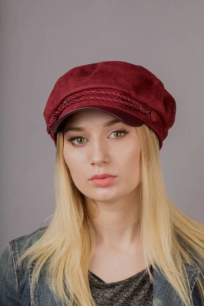 Retrato de uma bela jovem em uma cobertura para a cabeça elegante com maquiagem natural em um fundo cinza . — Fotografia de Stock