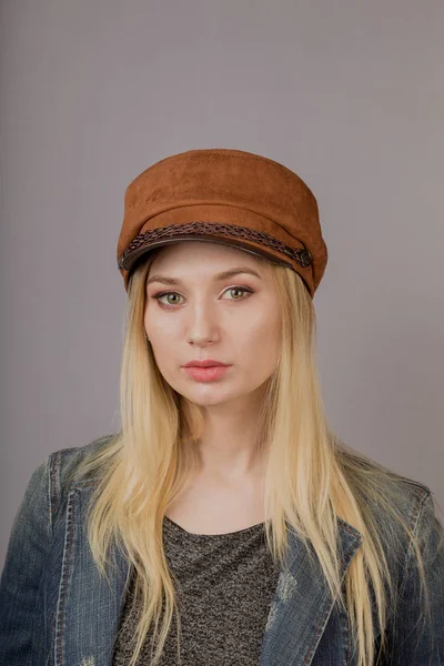 Portret van een mooi jong meisje in een stijlvolle hoofdtooi met natuurlijke make-up op een grijze achtergrond. — Stockfoto