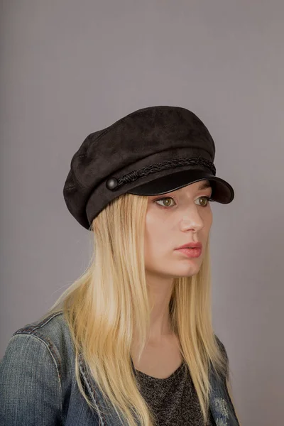 Retrato de uma bela jovem em uma cobertura para a cabeça elegante com maquiagem natural em um fundo cinza . — Fotografia de Stock