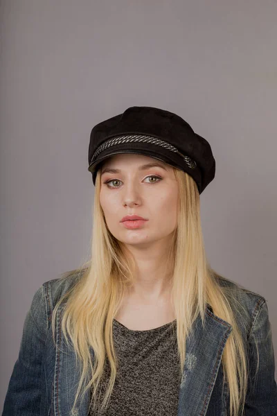 Retrato de uma bela jovem em uma cobertura para a cabeça elegante com maquiagem natural em um fundo cinza . — Fotografia de Stock