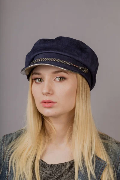 Retrato de uma bela jovem em uma cobertura para a cabeça elegante com maquiagem natural em um fundo cinza . — Fotografia de Stock