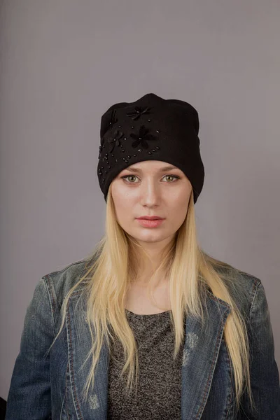 Portret van een mooi jong meisje in een stijlvolle hoofdtooi met natuurlijke make-up op een grijze achtergrond. — Stockfoto