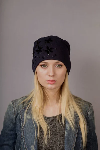 Portret van een mooi jong meisje in een stijlvolle hoofdtooi met natuurlijke make-up op een grijze achtergrond. — Stockfoto