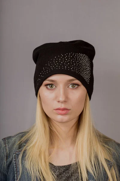 Portret van een mooi jong meisje in een stijlvolle hoofdtooi met natuurlijke make-up op een grijze achtergrond. — Stockfoto