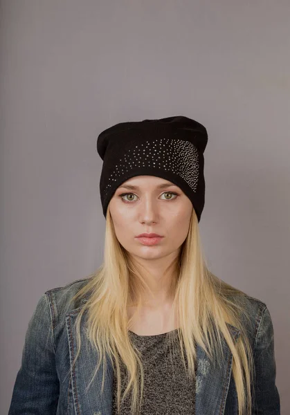 Portret van een mooi jong meisje in een stijlvolle hoofdtooi met natuurlijke make-up op een grijze achtergrond. — Stockfoto