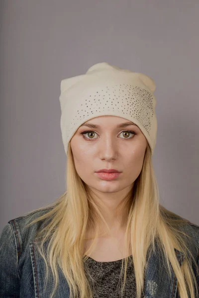 Portret van een mooi jong meisje in een stijlvolle hoofdtooi met natuurlijke make-up op een grijze achtergrond. — Stockfoto