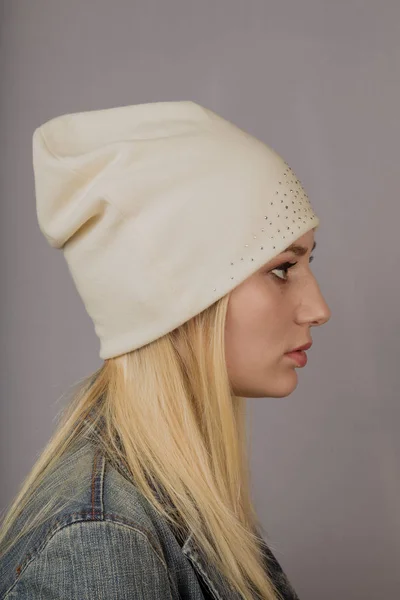 Portret van een mooi jong meisje in een stijlvolle hoofdtooi met natuurlijke make-up op een grijze achtergrond. — Stockfoto