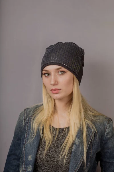 Portret van een mooi jong meisje in een stijlvolle hoofdtooi met natuurlijke make-up op een grijze achtergrond. — Stockfoto