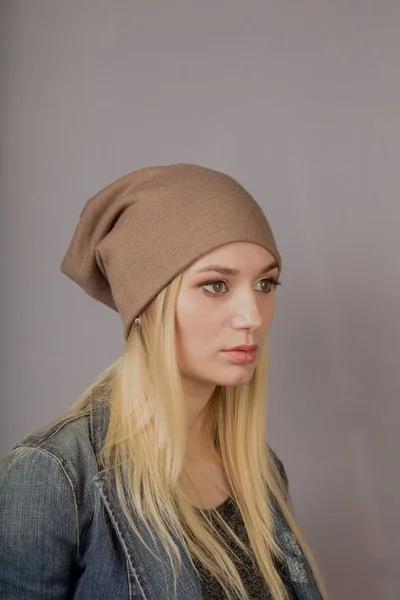 Portret van een mooi jong meisje in een stijlvolle hoofdtooi met natuurlijke make-up op een grijze achtergrond. — Stockfoto