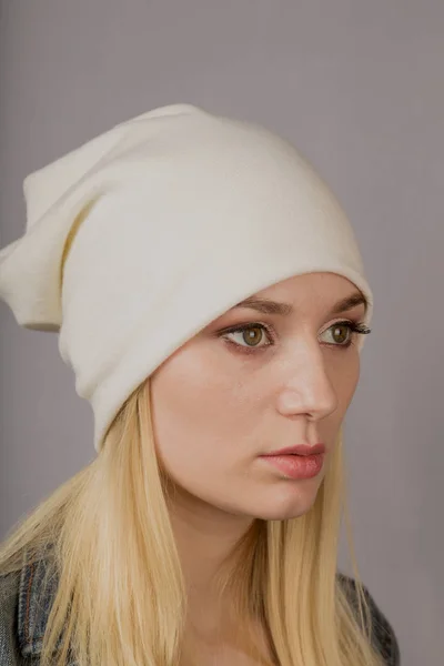 Portret van een mooi jong meisje in een stijlvolle hoofdtooi met natuurlijke make-up op een grijze achtergrond. — Stockfoto