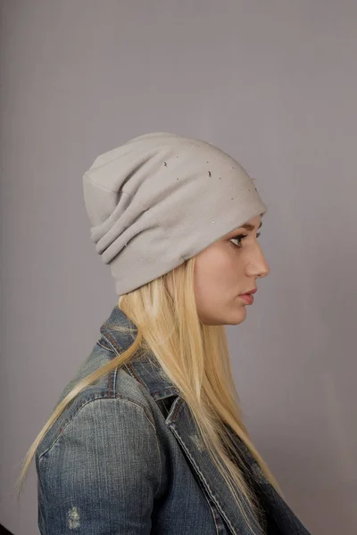 Portret van een mooi jong meisje in een stijlvolle hoofdtooi met natuurlijke make-up op een grijze achtergrond. — Stockfoto