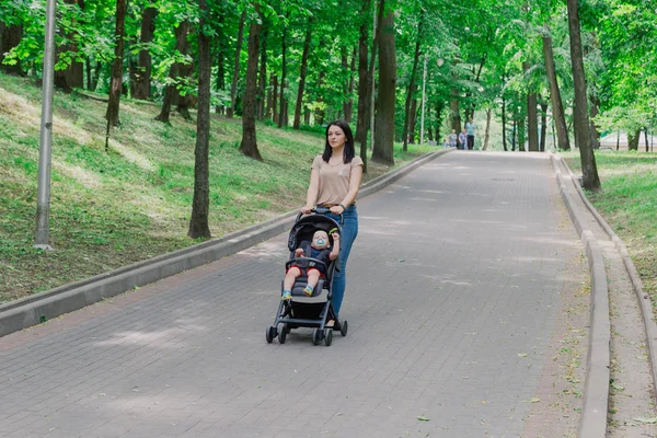 Bebek arabasında çocuklu güzel kadın bir yaz parkında yürüyor.