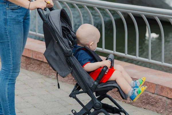 Красивая женщина с ребенком в коляске гуляет по летнему парку . — стоковое фото