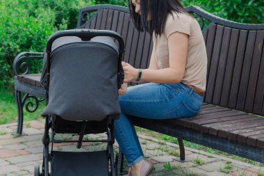 Güzel anne yaz aylarında güneşli bir günde bebek arabası bir bebek ile bir bankta oturur.