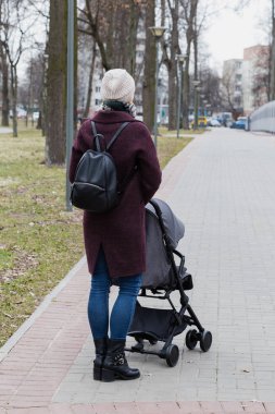 Kız bir bebek arabası ile parkta yürüyor.