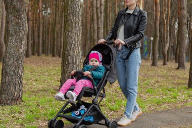 Genç anne bebek arabasında bir bebekle yürüyor..