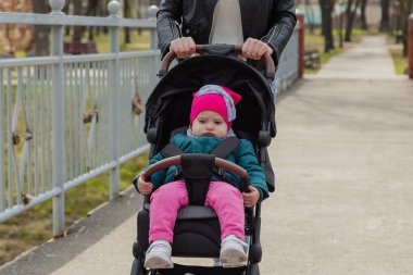 Genç anne bebek arabasında bir bebekle yürüyor..