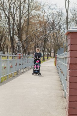 Genç anne bebek arabasında bir bebekle yürüyor..
