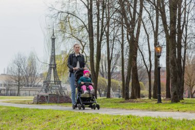 Genç anne bebek arabasında bir bebekle yürüyor..