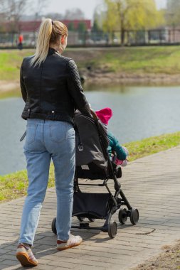 Genç anne bebek arabasında bir bebekle yürüyor..