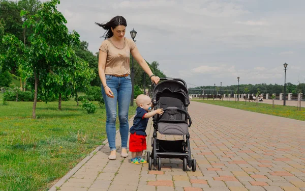 В парке прогуливается молодая мать с ребенком рядом с коляской . — стоковое фото