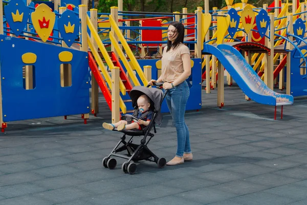 Молодая мама с ребенком в коляске на детской площадке. — стоковое фото