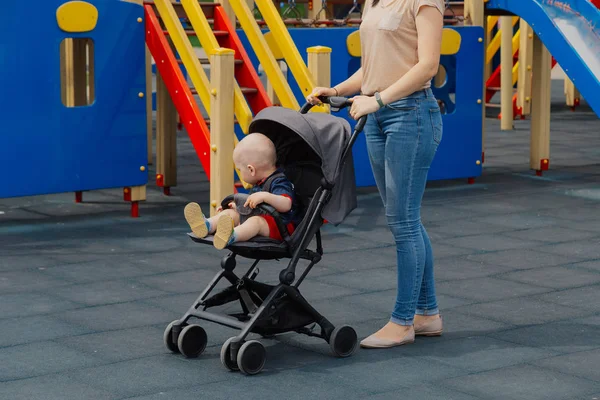 Молодая мама с ребенком в коляске на детской площадке. — стоковое фото