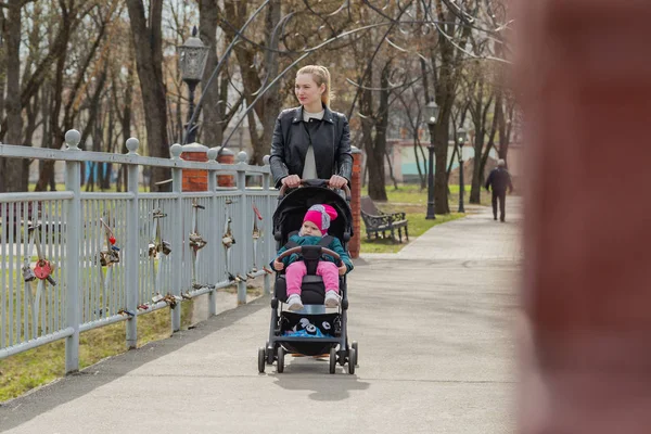 Jovem mãe caminha com um bebê em um carrinho . — Fotografia de Stock