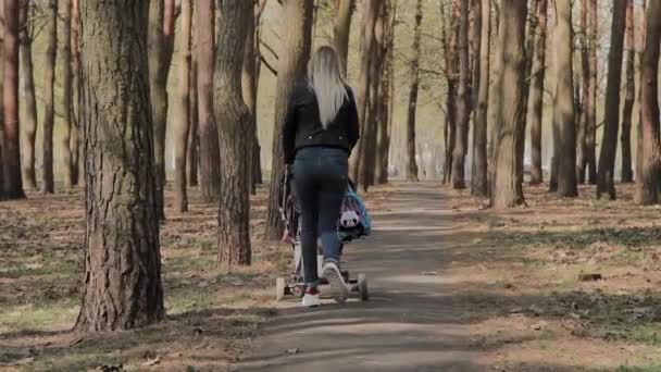 Gyönyörű nő sétál a kislánya, és nyomja push babakocsi parkban. Anya sétál egy babakocsi a parkban — Stock videók