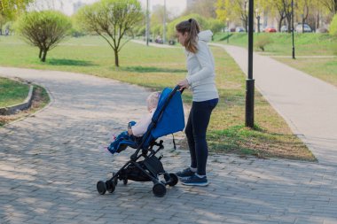 Young mother with a baby in a stroller in a summer park.