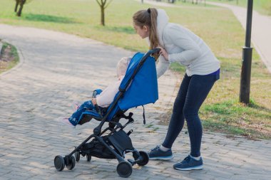Young mother with a baby in a stroller in a summer park.