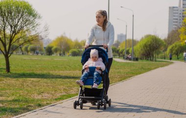 Young mother with a baby in a stroller in a summer park.