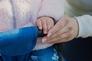 Genç bir anne bebek arabasında oturan bir çocuğun elini tutar..