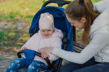 Bebek arabası yla genç bir anne güneşli bir günde bankta oturur..