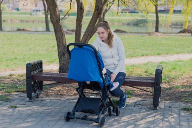 Bebek arabası yla genç bir anne güneşli bir günde bankta oturur..