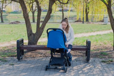 Bebek arabası yla genç bir anne güneşli bir günde bankta oturur..