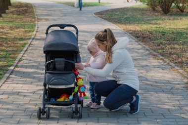 Genç bir anne bebek arabası yuvarlayan bir çocukla yürüyor..