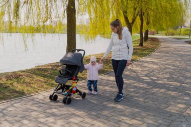 Genç bir anne bebek arabası yuvarlayan bir çocukla yürüyor..