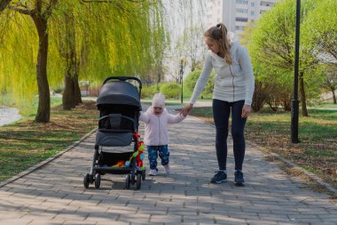 Genç bir anne bebek arabası yuvarlayan bir çocukla yürüyor..