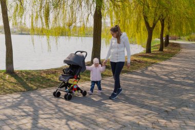 Genç bir anne bebek arabası yuvarlayan bir çocukla yürüyor..